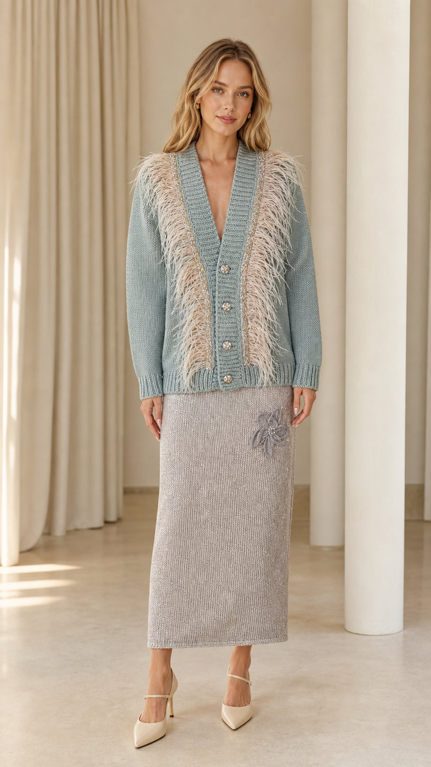 Front view of woman wearing dusty blue feather trim cardigan paired with a grey knit skirt