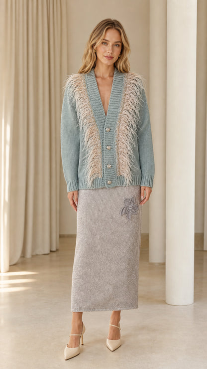 Front view of woman wearing dusty blue feather trim cardigan paired with a grey knit skirt