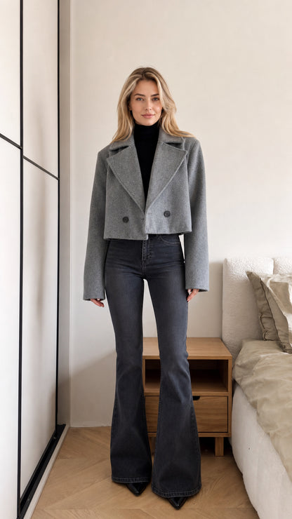 Front view of model wearing grey cropped double-breasted jacket with black turtleneck and flare jeans