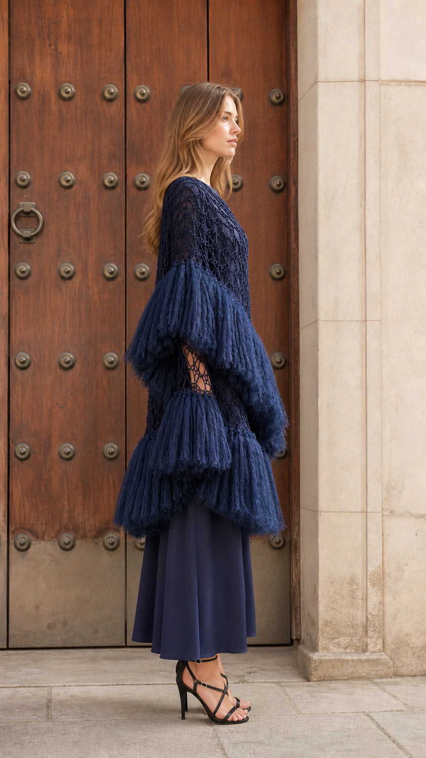 Side profile view showing dramatic volume and layered fringe sleeves of navy blue poncho top