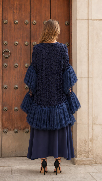 Back view of navy blue openwork crochet poncho with tiered fringed hem