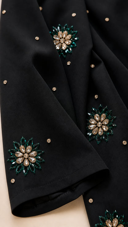 Close-up detail of emerald green and gold crystal floral embellishments on black fabric