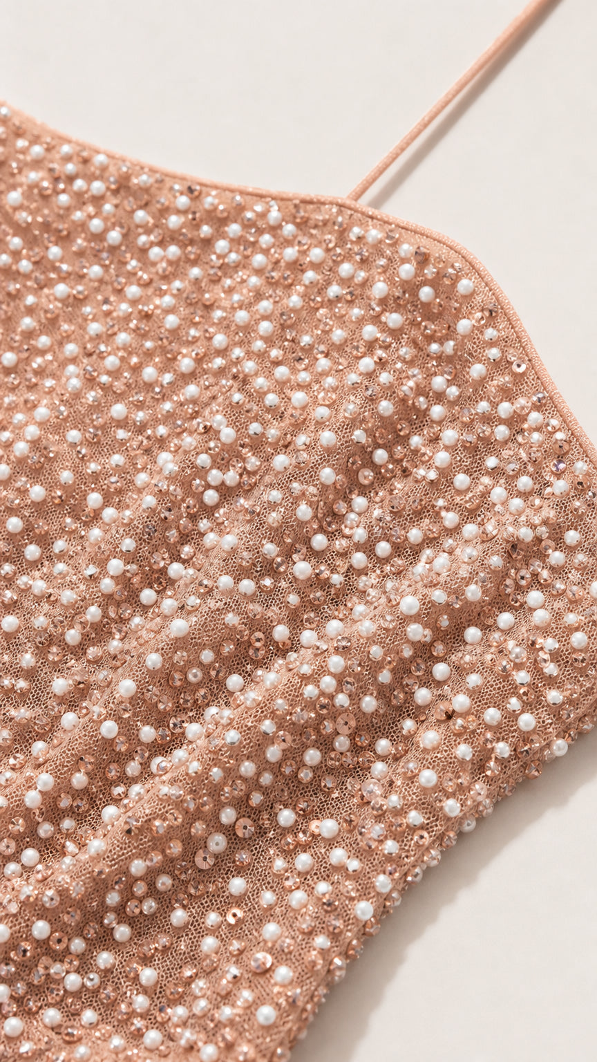 Close-up detail of textured pearl beading and delicate spaghetti strap on blush pink fabric