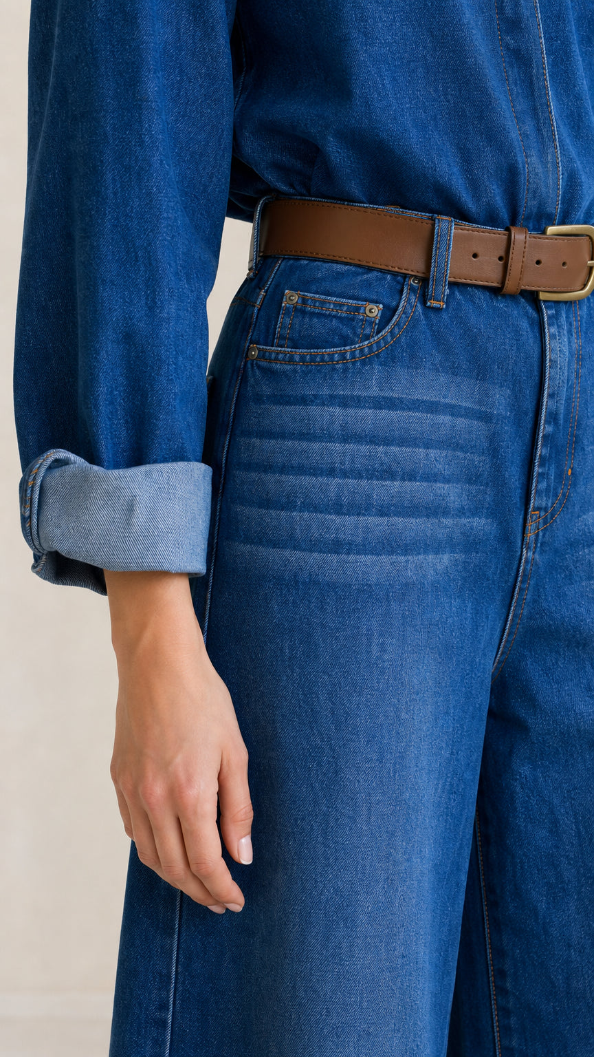 Close-up of waistband, belt, pocket details, and rolled cuffs on denim jumpsuit