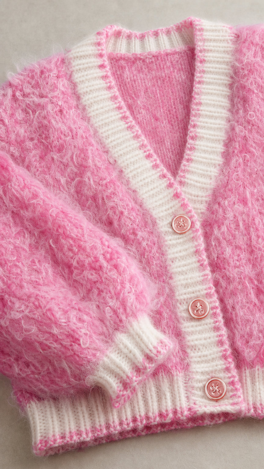 Close-up detail of pink fuzzy knit fabric, contrast ribbed trim, and buttons
