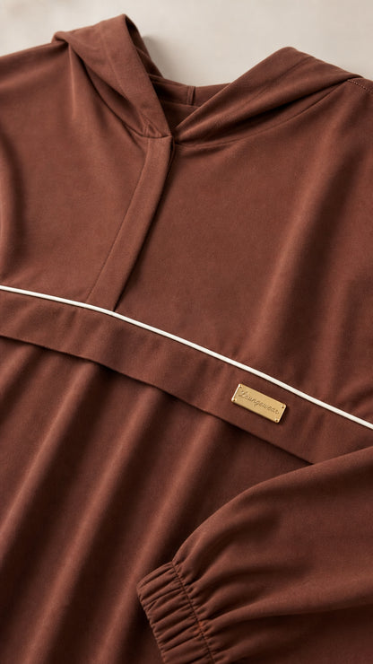 Close-up detail of brown knit fabric showing hooded placket, piping trim, and brand accent