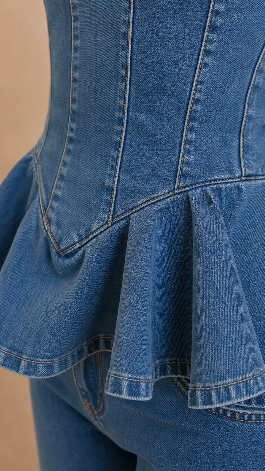 Close-up detail of structured corset seaming and flared peplum ruffle on blue denim top