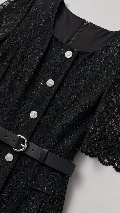 Close-up detail of black lace fabric, metallic buttons, and belted waistline