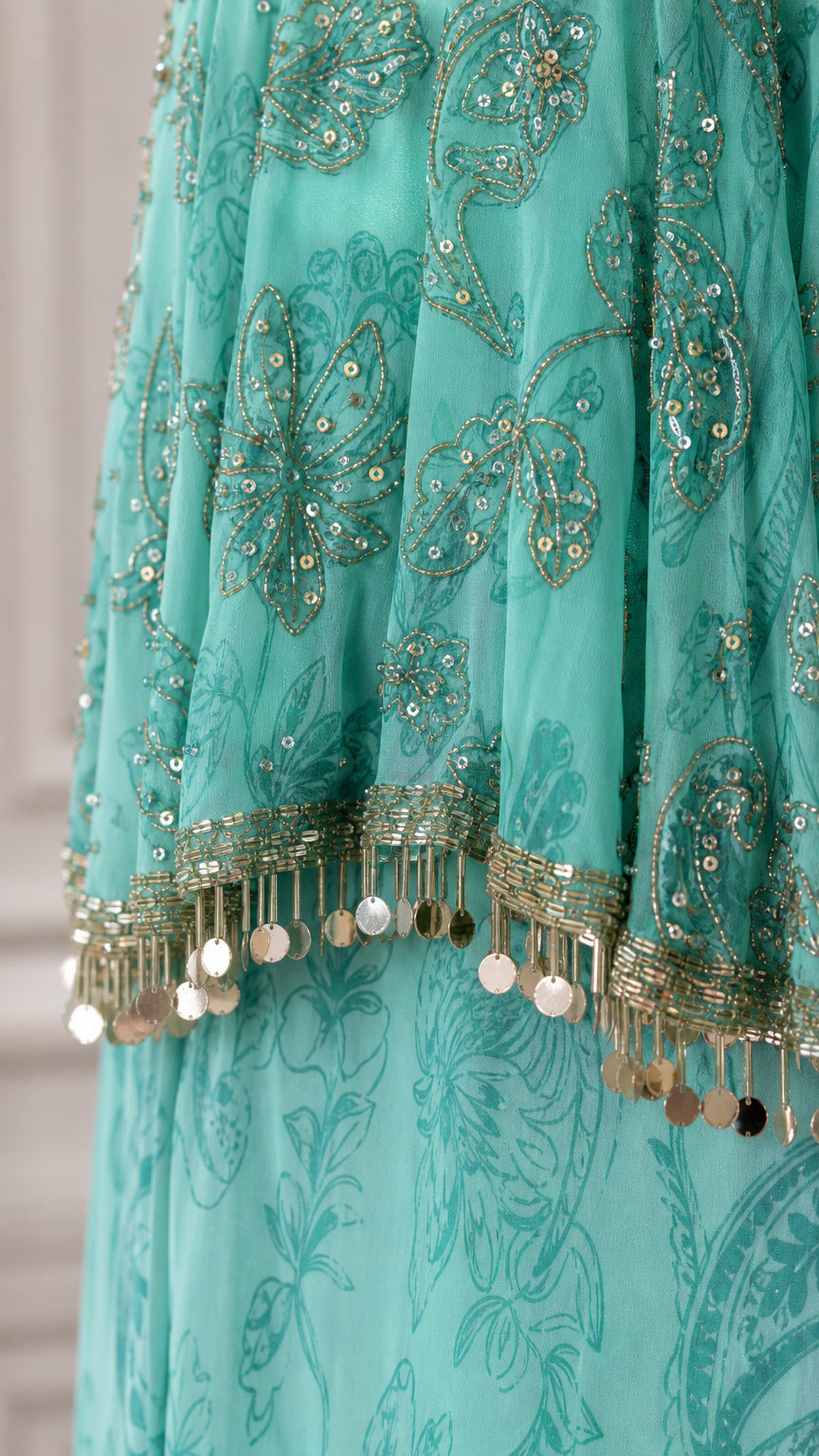 Close-up detail of turquoise embroidered fabric with sequins and metallic coin fringe trim