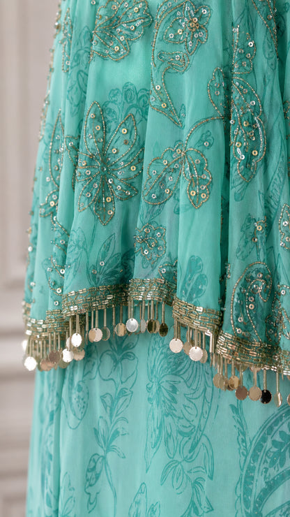 Close-up detail of turquoise embroidered fabric with sequins and metallic coin fringe trim