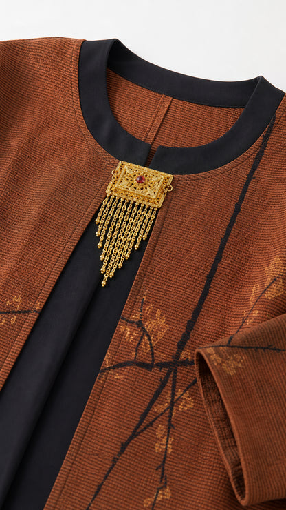 Close-up detail of textured fabric, black collar binding, and gold pendant brooch with tassels