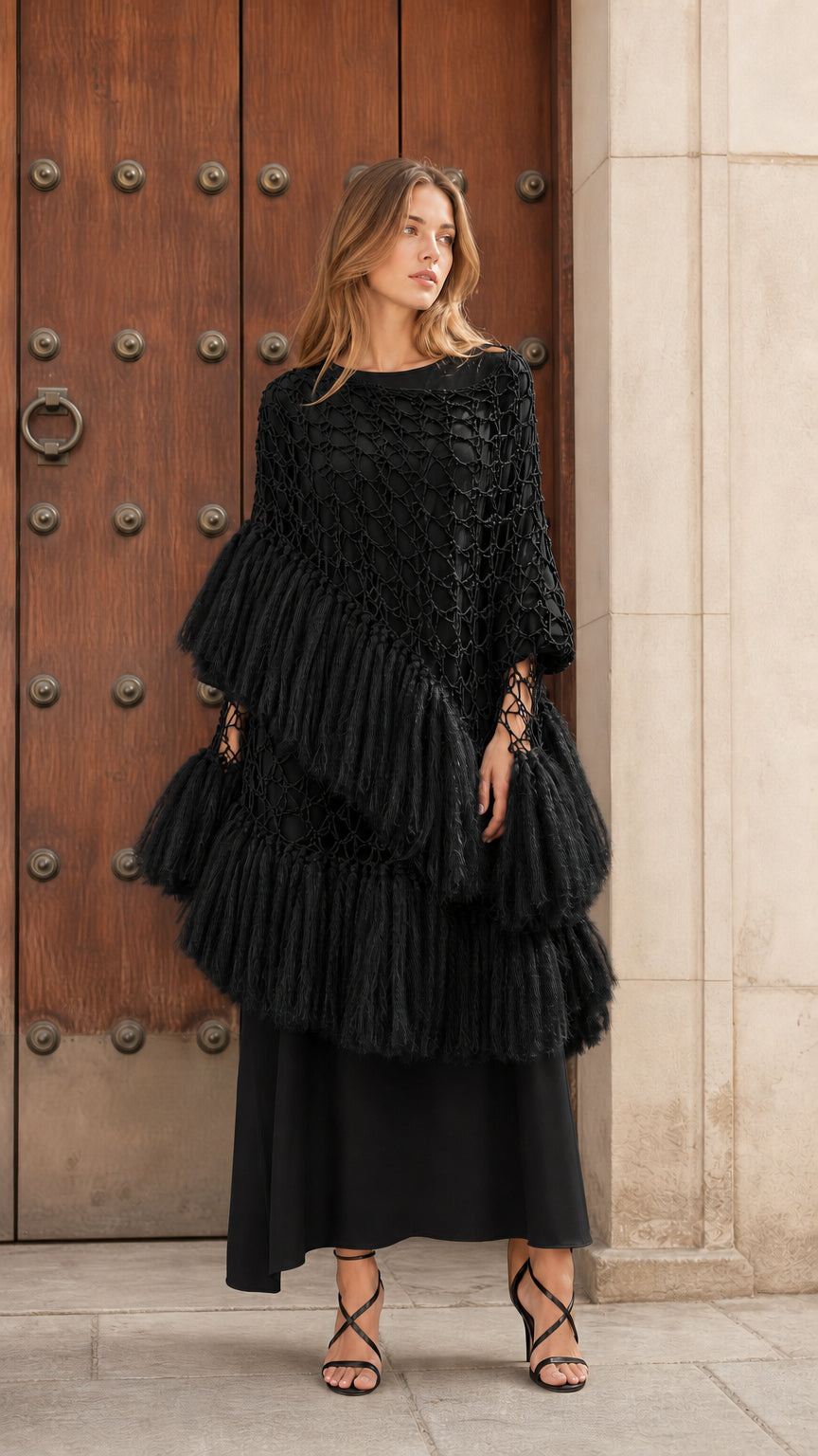 Front view of black tiered fringe crochet poncho top styled over a black maxi dress