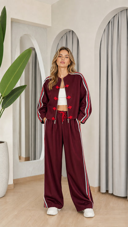 Model wearing burgundy two-piece tracksuit set with red accents