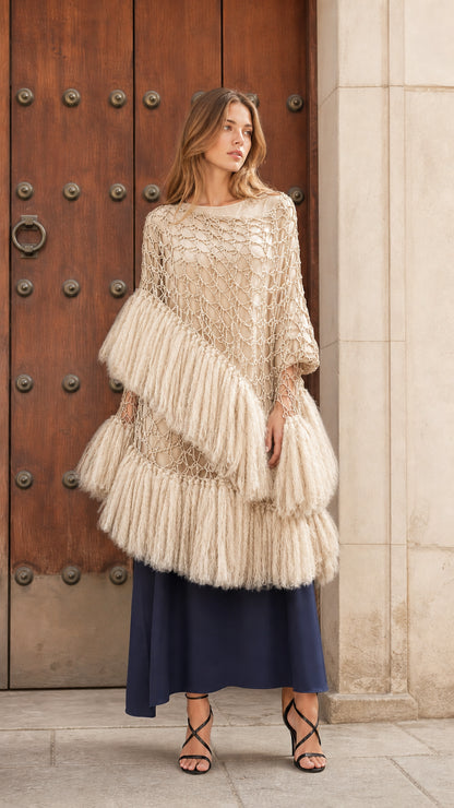 Front view of beige cream tiered fringe crochet poncho top layered over a navy skirt
